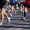 A group of people are running in a race.  Only their legs are visible.  They are all wearing short pants and T-shirts.  They are also wearing running shoes.  On the right side of the ground, the shadows of spectators are visible.